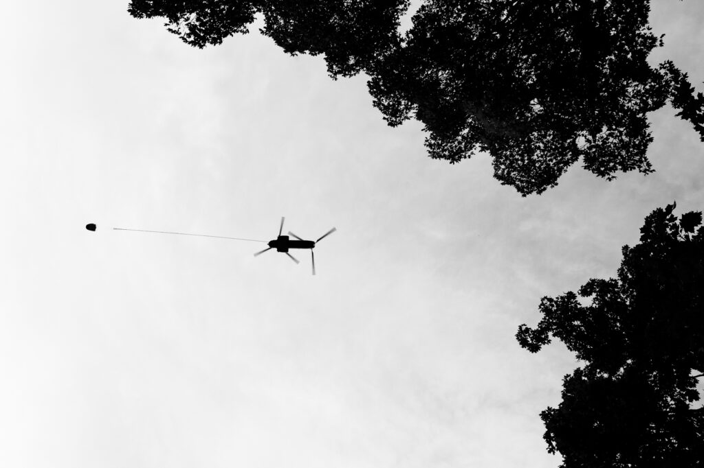 An aerial firefighting helicopter flies overhead carrying a bucket of water.